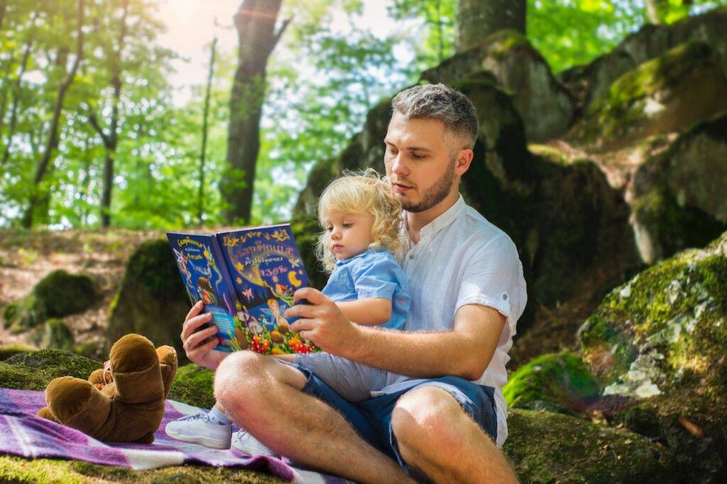 A Man and his child enjoying a book together - Hobbies For Dads