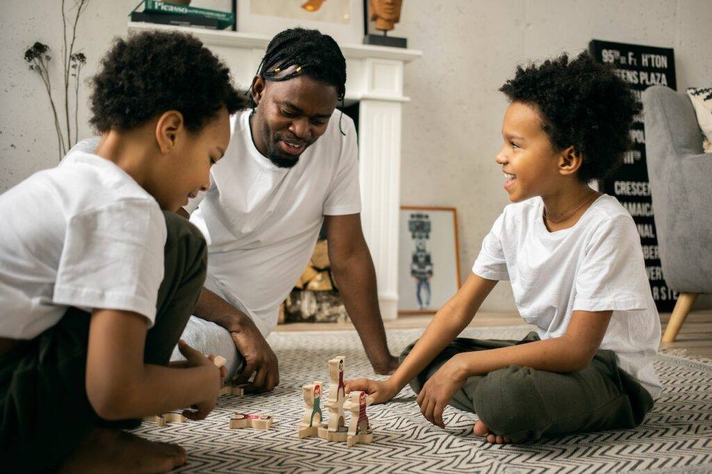 A Man and his two kids playing a board game - Hobbies For Dads